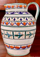 Front view of the Italian stoneware faience jug showing detailed hand-painted designs in orange, blue, and green color scheme.