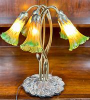 Photo of the entire 5-arm table lamp showing the metal base and five lit tulip-shaped glass shades with gradient colors from yellow to green.