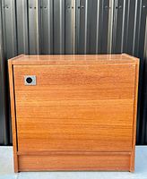 Front view of the teak side console cabinet showing the minimalist design, rectangular shape, and stainless steel inset circular pull handle on the door.