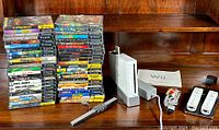 Overview of lot showing two stacks of GameCube game cases, Wii console, sensor bar, stand, manual, cables, remotes, and charger dock.