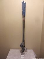 Photo shows a bundle of nine golf clubs with blue grips, consisting of six irons and three woods, standing against a plain wall.