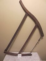 Front view of the antique wooden bow saw showing the metal blade and wooden curved frame, with visible tension wire and handle.