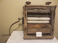 Front angle view of antique wooden washer-wringer showing hand crank and dual rollers with wear and paint chipping.