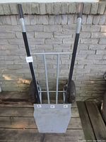 Gray heavy-duty dolly with black handles and two large pneumatic tires leaning against a brick wall.