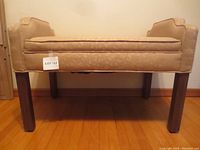 Front-side view of tan upholstered settee bench with wooden legs showing size and shape