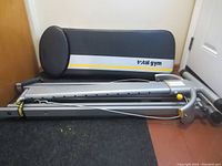 Main gym frame folded with padded seat and backrest visible, grey metal structure with Total Gym branding and yellow accent line.