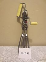 Photo of vintage Maynard mechanical hand mixer egg beater showing dual metal blades and yellow handles on crank and top grip