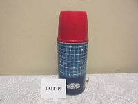 Full view of the vintage Thermos showing body with blue and white grid pattern and red cup cap, standing upright