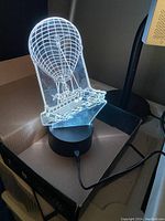 3D Fortnite Battle Bus light illuminated with white light on black base and power connected, displayed with original box in background.