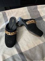 Pair of Croc brand heeled slip-on shoes, black with leopard print accent, size 7, displayed on a beige and gray fabric surface.