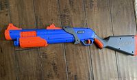 Side view of blue and orange Nerf blaster with grey stock, laid flat on wooden floor