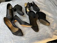 Four pairs of ladies black shoes including a pair of slingbacks and three pairs of closed heels displayed on a light surface.