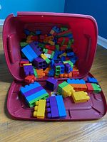 Half bin full of assorted colorful Mega Bloks building blocks, various sizes and colors poured out inside a red plastic bin.