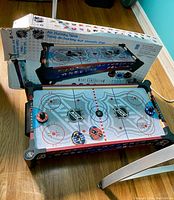 Mini NHL air hockey table with NHL logos, mallets, pucks, and its original box.