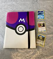 Front view of the Pokémon trading card binder with one large and three regular Pokémon cards shown next to it.