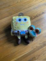 Two plush toys of SpongeBob and Gary on a wooden floor showing their front side.