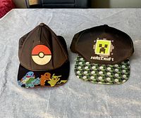 Two youth baseball caps side-by-side on a light-colored fabric surface, showing front panel and brim designs clearly.