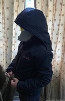 Dark water-repellent youth jacket worn by a figure, showing detachable hood and zipper front.