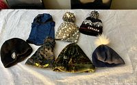 Photo showing 7 youth winter hats, assorted colors and styles, laid out flat for display.