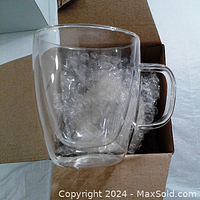 Photo showing one double wall glass cup held in front of an open cardboard box with bubble wrap inside.