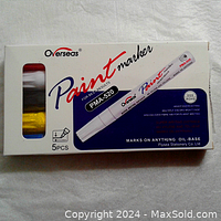 Front view of the closed box showing the five colored paint markers visible through the left window and product branding and specs on front of the box.