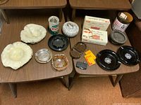 Full lot overview showing all ashtrays, lighter, match books, papers, and ceramic jar on two wooden tables.