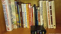 Photo of bookshelf showing assorted books on medical guides, food preservation, and stain removal, along with a vintage Equalizer noise maker device front panel