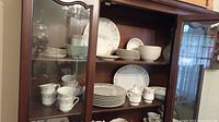 Full view of china cabinet shelves showing stacked china pieces including plates, bowls, cups, and serving pieces.