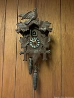 Full view of wooden cuckoo clock on wood panel wall showing body, weights, and face.