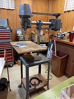 Front‐right angle of the drill press on its metal stand in the workshop.
