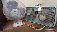 Two fans side by side on floor showing Electrohome Long Life rectangular metal frame floor fan and white Super 18" table fan