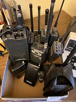 Box containing multiple handheld radio transmitters with antennas and some accessories including holsters.