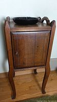 Front view of vintage wooden smoking table with cabinet door and black ashtray on top.