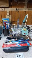 Photo showing Wahl cordless soldering iron on stand, Cold Heat soldering iron, solder wire spools, hemostat, and safety glasses on countertop under power strip