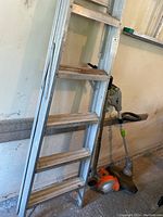Aluminum step ladder next to Black & Decker edger and EarthWise string trimmer positioned against wall.
