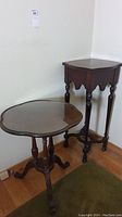 Two small wooden tables positioned together. One a corner table with turned legs, the other a scalloped top round table with glass top and carved legs.