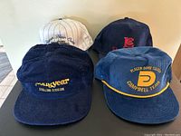 Four men's vintage hats displayed together on a black surface; two corduroy hats in front and two fabric hats in back