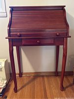 View of closed roll top desk showing tambour style curved top, single drawer below, and four curved legs.