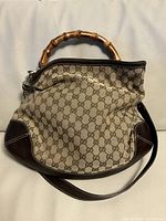 Front view of Gucci monogram canvas bag with bamboo handle and leather shoulder strap