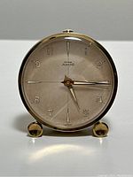 Front view showing clock face with Cyma Amic branding and brass frame