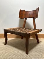Angled view of chair showing wooden frame, carved backrest and woven seat