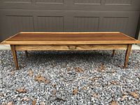 Front view of full coffee table on gravel background showing walnut top and lighter wood frame with tapered legs.