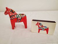 Photo of the red hand-painted Dalecarlian horse figurine with the matching box of matches on a white surface