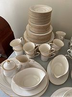 Stack of various sized Noritake plates with teacups and gravy boats in front, showing gold and gray swirl design with gold rims