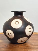 Front angle of round Peruvian pottery vase showing off-white circles with concentric smaller circles on dark background.