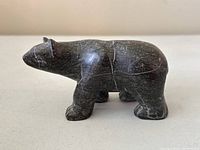 Side view of dark soapstone polar bear carving with white veining visible.