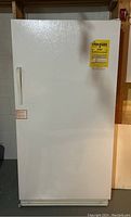Front view of the white upright freezer with EnergyGuide label and vertical handle, showing door and safety lock.