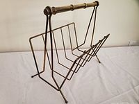 Front and side view of vintage brass magazine rack showing tubular handle and wire dividers.