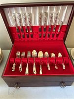 Open wooden vintage box showing knives secured vertically in the lid with red and white lining and forks and spoons neatly arranged on the base red velvet insert.