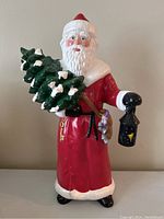 Full view of vintage ceramic Santa Claus figure holding green Christmas tree and black lantern.
